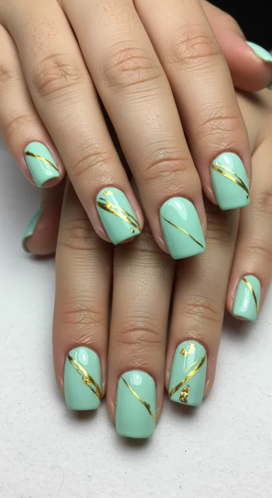 Mint green nails with a thin gold stripe running diagonally or horizontally, adding a touch of elegance. ✨