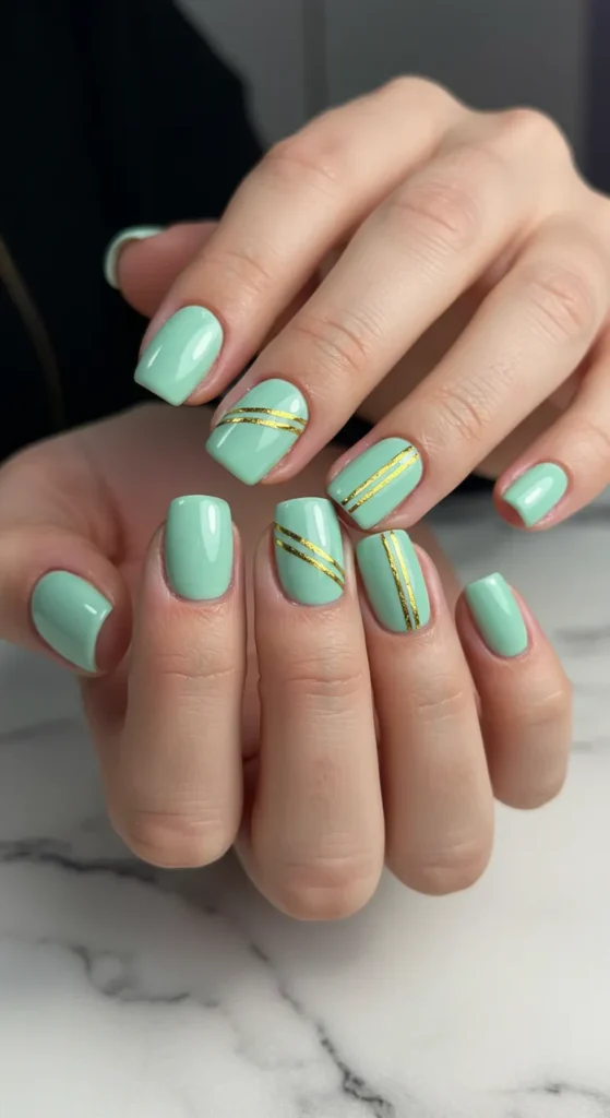 Mint green nails with a thin gold stripe running diagonally or horizontally, adding a touch of elegance. ✨